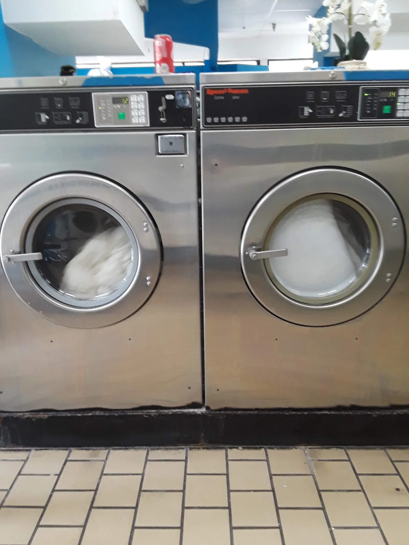 Close-up of two large stainless-steel front-load washing machines with laundry tumbling inside, viewed straight on.